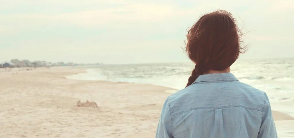 Persona de espaldas contemplando el mar desde la playa